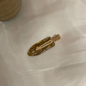 Detailed close-up of the amber tortoiseshell resin hair clip on white textured fabric