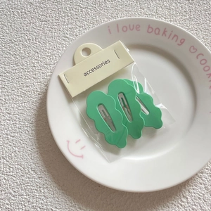Three pieces of mint green wavy bobby pins in original packaging on a white plate