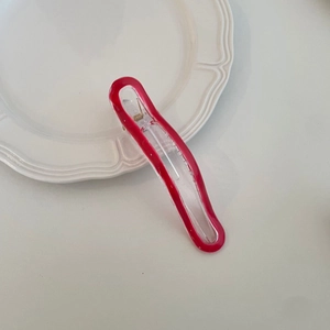 Macro detail of wave-shaped acrylic hair clip with red border and metal spring mechanism