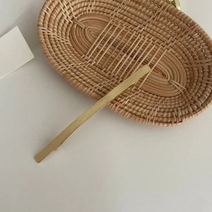 Minimalistische goldene Metallhaarklammer mit gebürsteter Textur auf Rattan-Hintergrund