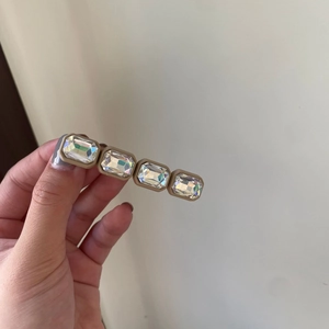 Detailed view of hand holding a hair clip with four rectangular clear crystals