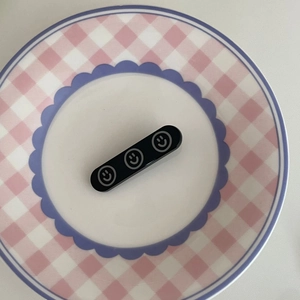 Barrette à cheveux noire minimaliste avec motifs smiley sur une assiette décorative