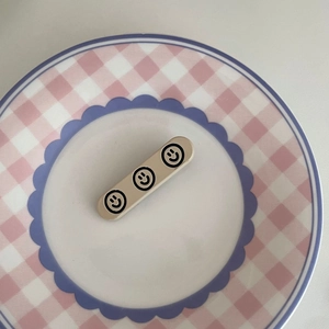 Barrette à cheveux crème minimaliste avec trois motifs de smileys noirs sur une assiette