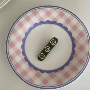 Vue détaillée d'une pince à cheveux rectangulaire vert foncé avec motifs de smileys blancs