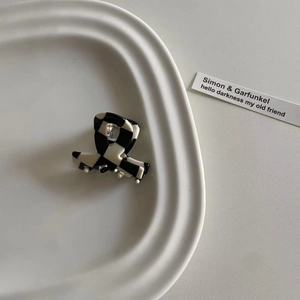 Mini-Haarklammer aus Acetat mit schwarz-weißem Karomuster auf einem Keramikteller