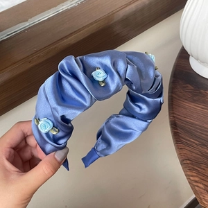 Détail macro du serre-tête en satin plissé bleu clair avec rose en tissu et feuilles dorées