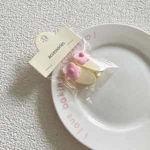 Detailed close-up of two floral matte hair clips on a white ceramic plate packaging display