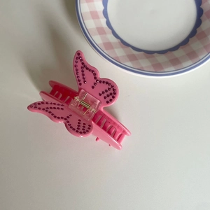 Détail d'une pince à cheveux papillon rose avec des strass brillants et ressort doré