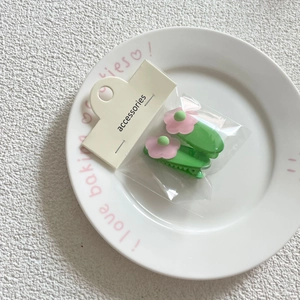 Detail view of two floral hair clips in light green and pink on a white ceramic plate