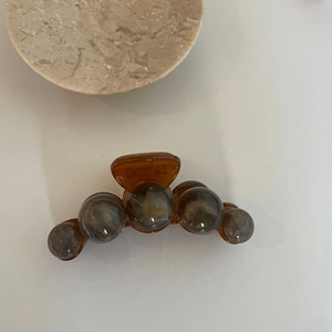Gros plan sur une pince à cheveux ambre avec perles marbrées grises sur plateau pierre