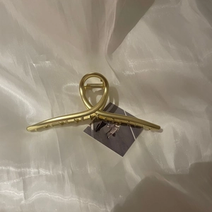 Détail d'une grande pince à cheveux en métal doré mat sur un fond de tissu blanc doux