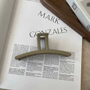 Macro detail of large matte khaki hair claw clip with metal spring on magazine background
