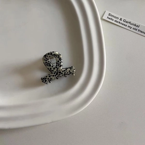Detail einer kleinen schwarz-weiß gepunkteten Acetat-Haarklammer auf einem Keramiktablett