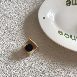 Detail of a beige matte small hair claw clip with a black smiley face emblem on top