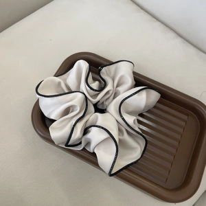 Elegant white satin scrunchie with black edge trim displayed on a tray for hair styling