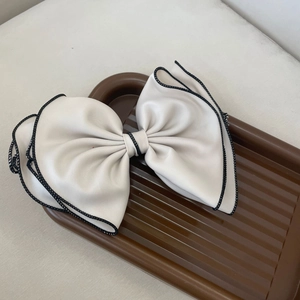 Detail view of a cream satin bow hair clip with contrasting black stitched edges