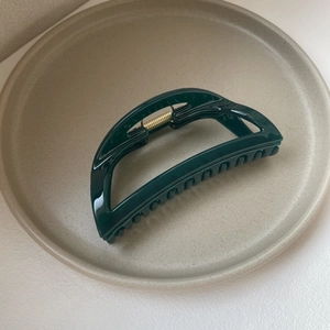 Detailed view of dark green glossy hair claw clip with golden metal spring on a beige plate