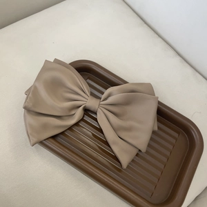 Detail view of a large mocha brown satin bow hair clip with tiered ribbon layers on a tray