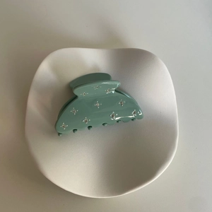 Détail de la pince à cheveux acétate vert Morandi avec strass sur plateau céramique
