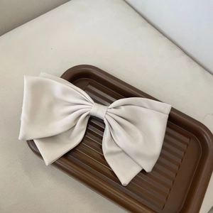 Detail of a large cream-colored bow hair clip made of premium matte leather in a tray