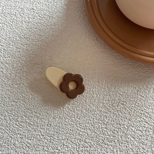 Minimalist flower hair clip in cream and coffee tones on a textured white surface