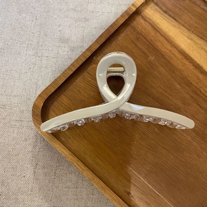 Detail of a large cream resin hair claw clip with cross design on a wooden tray