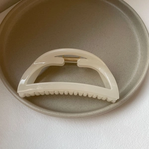 Detailed close-up of cream semi-circular hair claw clip with golden metal spring