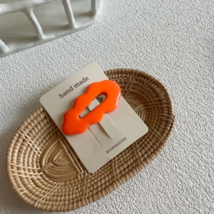 Close-up of an orange wavy resin hair clip on a handmade card in a woven basket