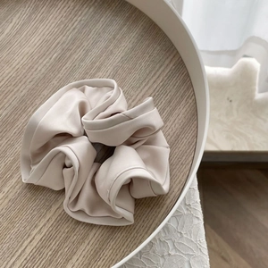 Elegant oversized beige satin scrunchie with ruffled edges in a wooden tray