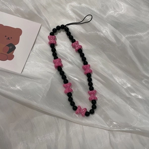 Detail of beaded phone strap with black glossy beads and pink bows on white silk