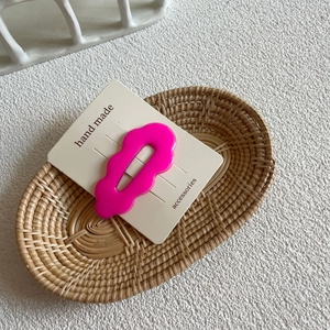 Cute wavy rose pink resin hair clip on a white card display in a woven basket