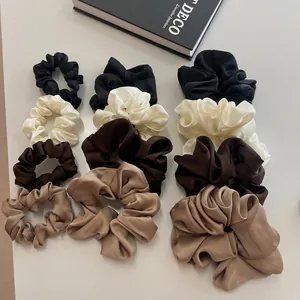 Satin silk scrunchies set in four earth tones and three sizes shown on a minimalist surface