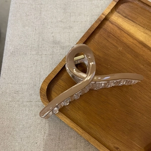Detail view of large cross claw hair clip in khaki and clear resin on wooden tray