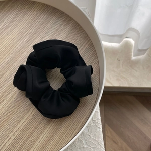 Close-up of black satin scrunchie with layered ruffles on a wooden tray with lace