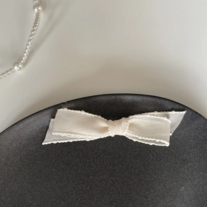 Détail d'une barrette noeud blanc cassé avec bords festonnés sur un plateau noir élégant