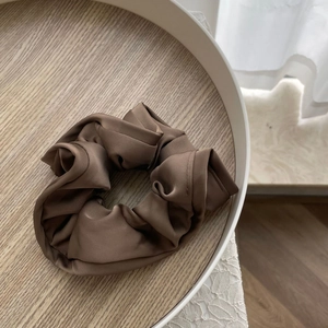 Detailed view of large brown satin scrunchie with elegant ruffles on a wooden tray