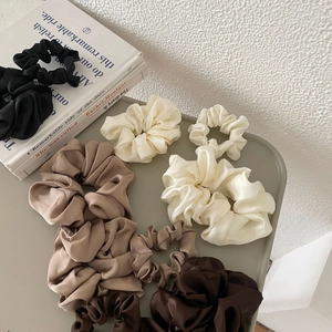 Elegant satin hair scrunchies in neutral tones displayed on a minimalist tray