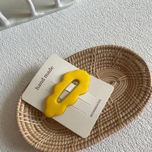 Detail of yellow wave-edged acrylic hair clip on a handmade display card in a woven basket