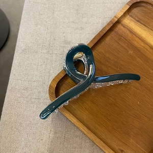 Detailed view of dark teal resin hair claw clip with twisted knot design on wooden tray