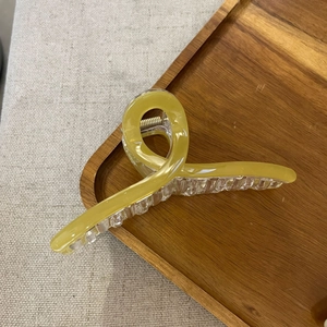 Close-up of mustard yellow resin hair claw clip with crossed spiral design on wood