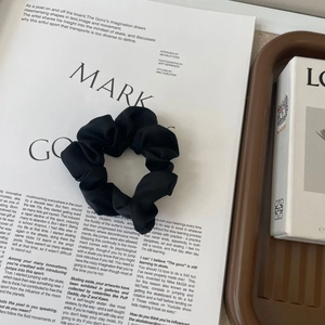 Detail of a large black satin scrunchie with soft fabric texture on a fashion magazine