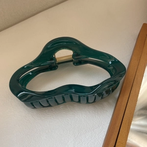 Gros plan d'une pince à cheveux vert émeraude avec ressort doré et design ondulé