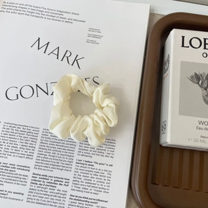 Detailed view of cream satin scrunchie placed on an artistic magazine with elegant props