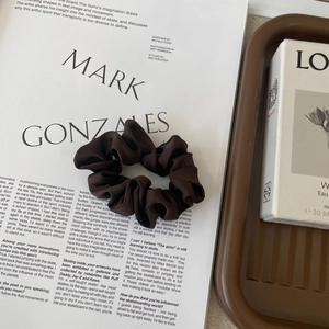 Detail of dark brown silk satin hair scrunchie with soft pleats on a stylish flat lay