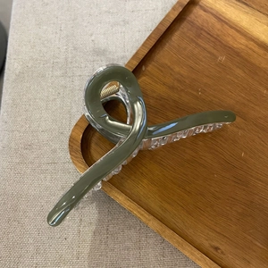 Green ice-glazed cross hair claw clip with twisted acrylic design on a wooden tray