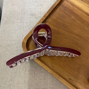 Close-up of a large burgundy cross hair claw clip with a transparent base on a wooden tray