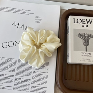 Detail of a creamy white satin silk scrunchie with smooth texture on a magazine