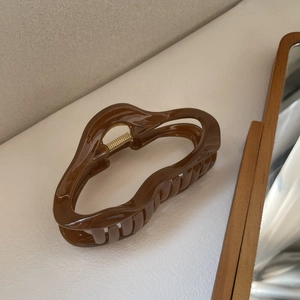Pince à cheveux géométrique ondulée marron, finition brillante et ressort doré sur table