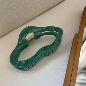 Détail de la pince à cheveux ondulée vert foncé avec fini brillant et ressort doré