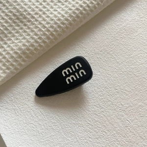 Dettaglio di un fermaglio per capelli nero a goccia con scritte min min su sfondo bianco